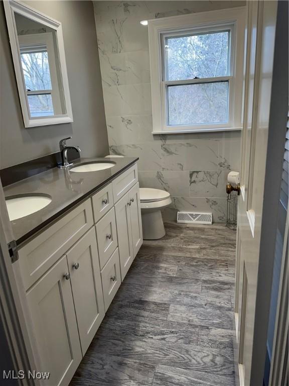 full bath featuring double vanity, toilet, visible vents, and a sink