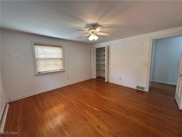 unfurnished bedroom featuring wood finished floors, baseboards, visible vents, ceiling fan, and a baseboard heating unit