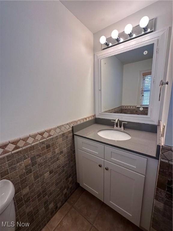 bathroom featuring a wainscoted wall, toilet, tile walls, vanity, and tile patterned floors