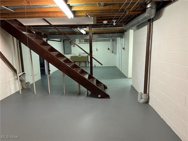 unfinished below grade area featuring electric panel, concrete block wall, and stairway