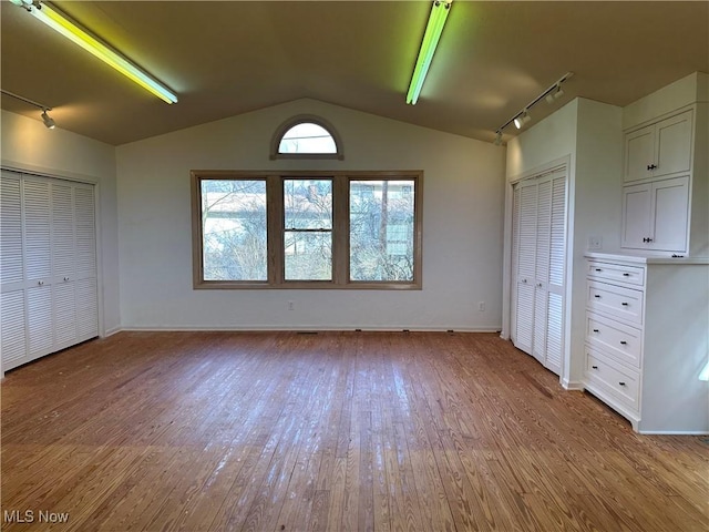 unfurnished bedroom featuring light wood finished floors, rail lighting, and vaulted ceiling