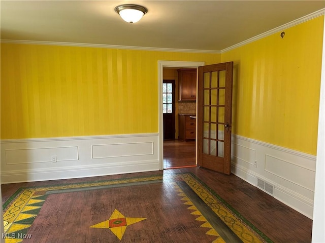 empty room featuring a wainscoted wall, dark wood-style flooring, and crown molding