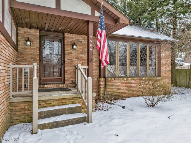 snow covered property entrance with brick siding