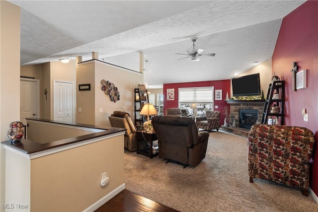 living area with a ceiling fan, wood finished floors, vaulted ceiling, a textured ceiling, and a stone fireplace