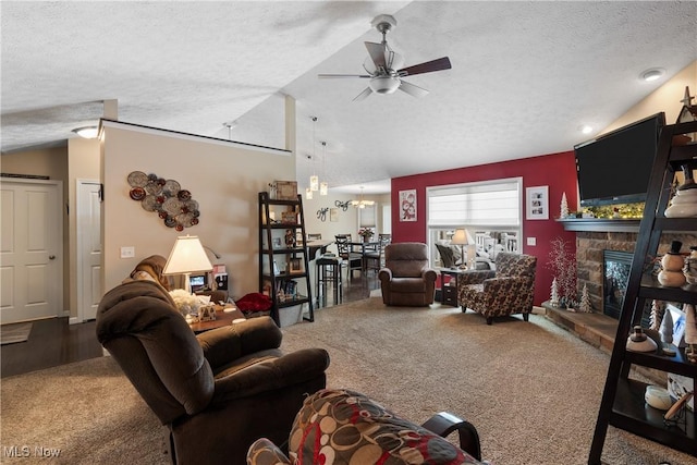 carpeted living area with ceiling fan, vaulted ceiling, a textured ceiling, and a stone fireplace