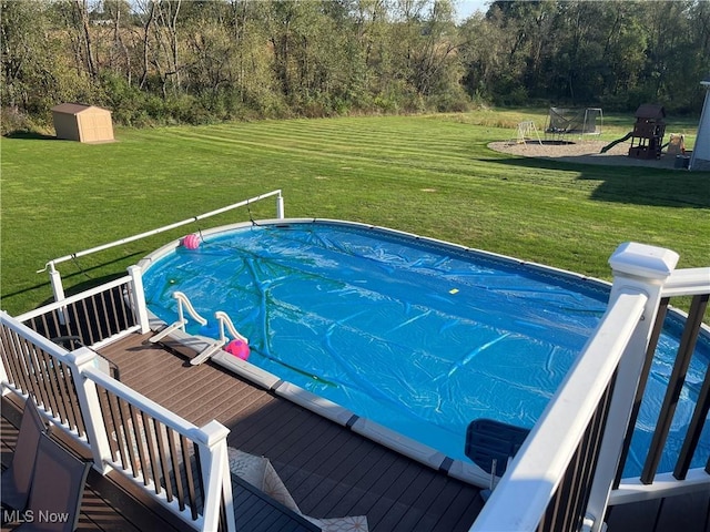 view of pool featuring a deck, an outdoor structure, a lawn, a covered pool, and a shed