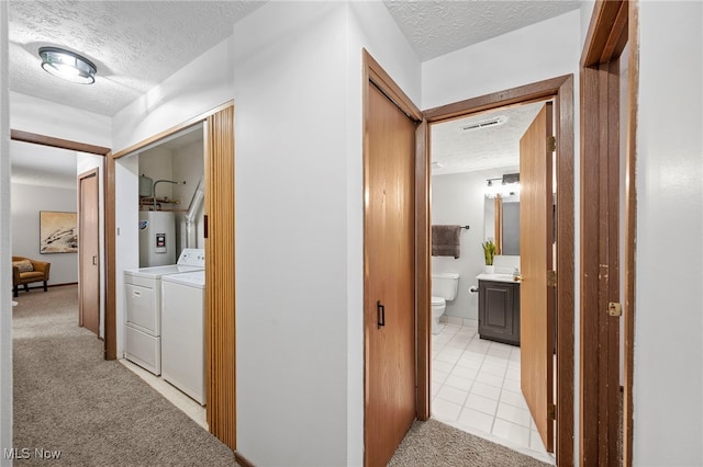 corridor featuring a textured ceiling, light colored carpet, separate washer and dryer, visible vents, and water heater