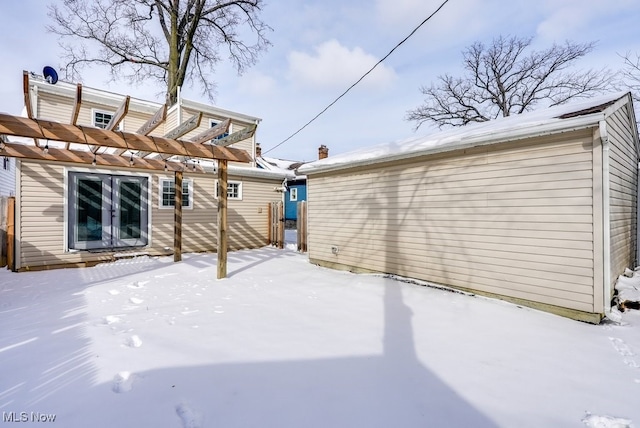 snow covered back of property with a pergola