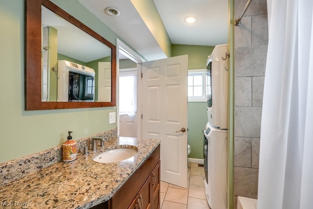 bathroom with stacked washer and clothes dryer, toilet, tile patterned flooring, walk in shower, and vanity