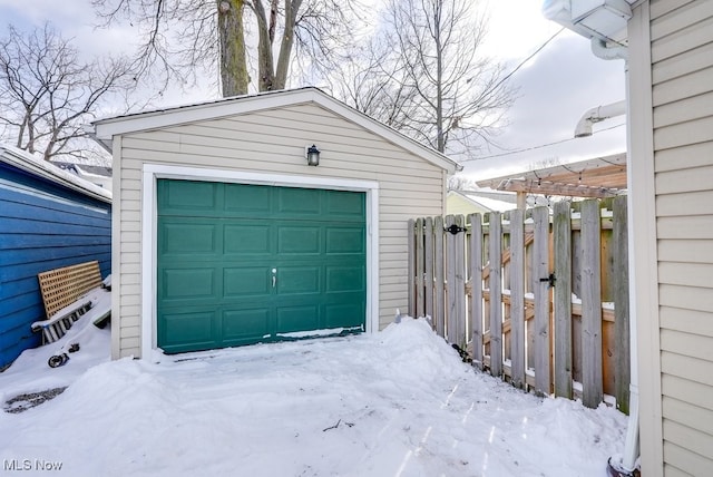 snow covered garage with a garage and fence