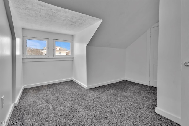 bonus room featuring a textured ceiling, vaulted ceiling, dark carpet, and baseboards