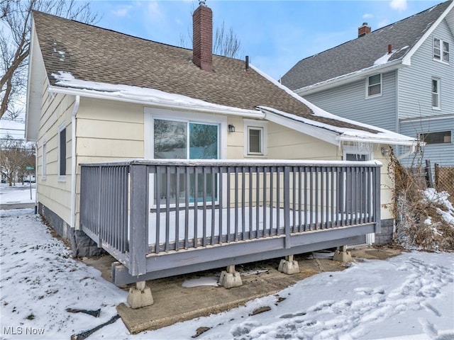 snow covered rear of property with covered porch, a chimney, and roof with shingles