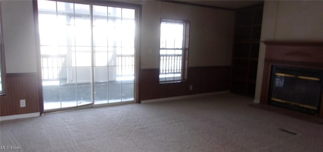 unfurnished living room featuring a wainscoted wall, carpet floors, a glass covered fireplace, and wooden walls