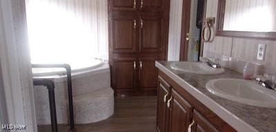 bathroom featuring wood finished floors, a garden tub, a sink, and double vanity