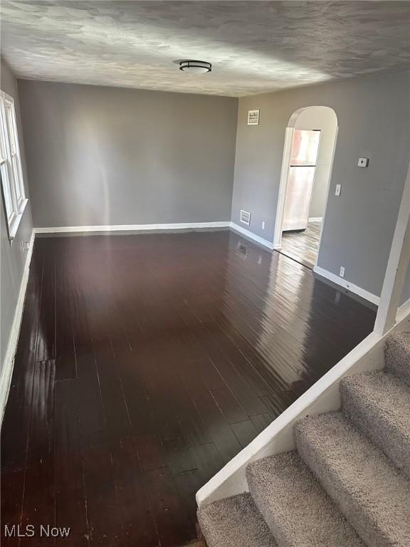 spare room featuring arched walkways, wood finished floors, and stairs