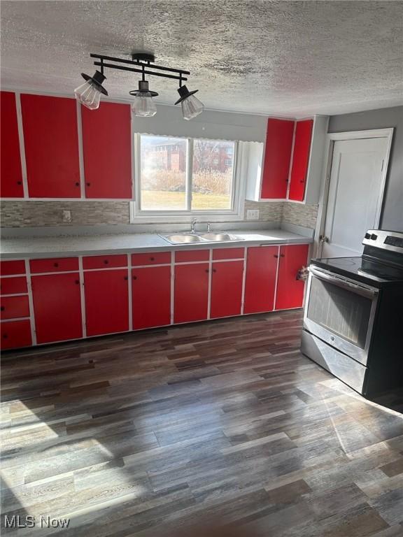 kitchen featuring electric range, red cabinetry, dark wood-style flooring, a textured ceiling, and a sink