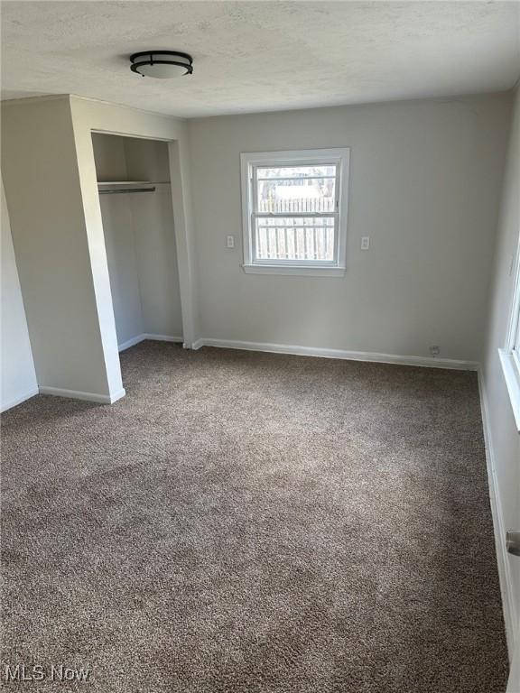 unfurnished bedroom featuring a textured ceiling, carpet floors, a closet, and baseboards