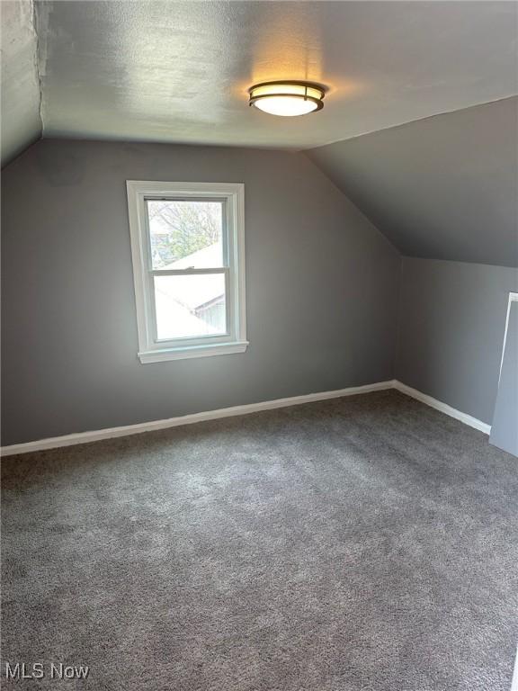 bonus room with carpet floors, lofted ceiling, a textured ceiling, and baseboards