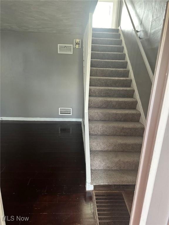 stairs with baseboards, visible vents, and wood finished floors