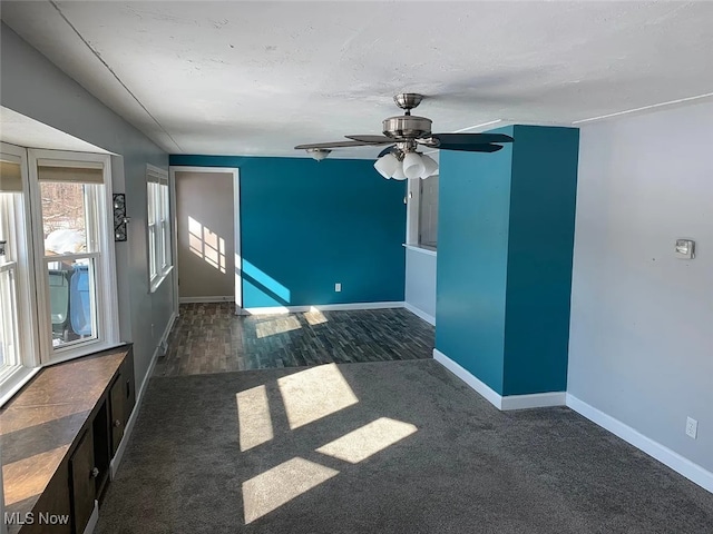 empty room featuring dark wood-type flooring, dark colored carpet, ceiling fan, and baseboards