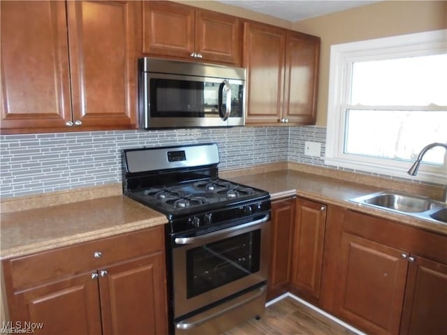 kitchen with a sink, light countertops, appliances with stainless steel finishes, backsplash, and brown cabinets