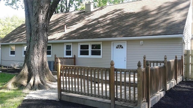 view of front of house with a deck, roof with shingles, and a chimney