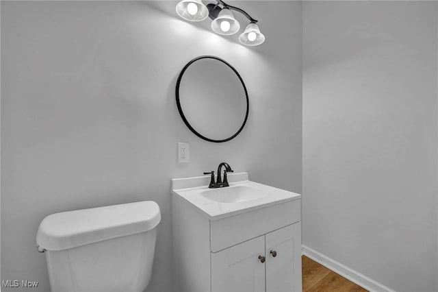 half bath with baseboards, vanity, toilet, and wood finished floors