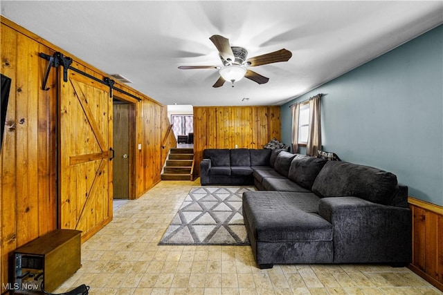 living room with visible vents, stairway, a barn door, ceiling fan, and wood walls