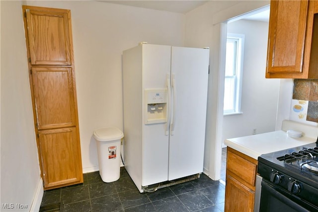 kitchen with brown cabinetry, white refrigerator with ice dispenser, light countertops, and black gas stove