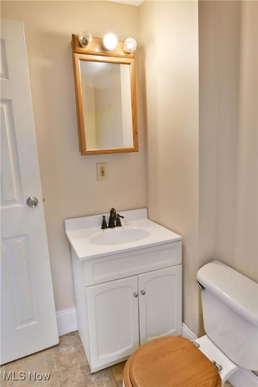 half bathroom with vanity, toilet, and baseboards