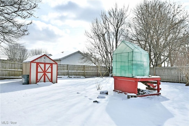 snowy yard with a storage unit, an outdoor structure, and a fenced backyard