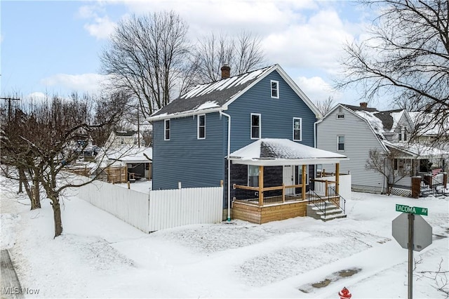 snow covered house featuring a porch and a chimney