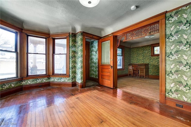 empty room with a textured ceiling, baseboards, wood finished floors, and wallpapered walls