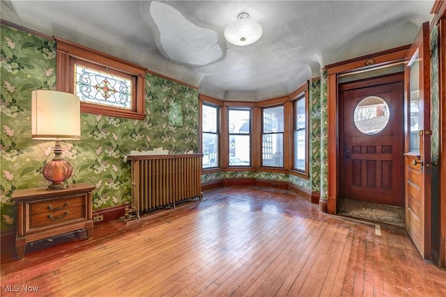 foyer entrance featuring baseboards, radiator, wood finished floors, and wallpapered walls