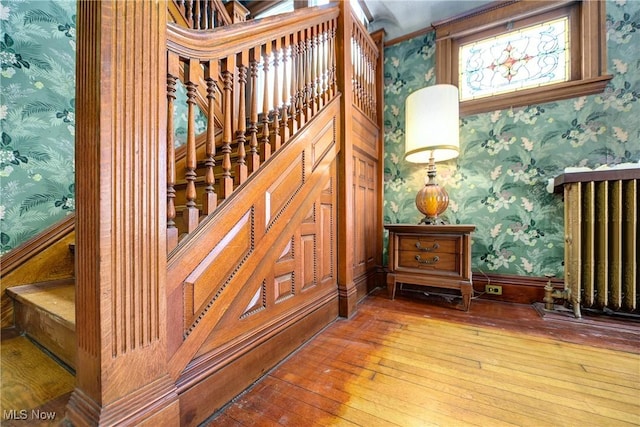 stairs with wood finished floors, radiator, baseboards, and wallpapered walls