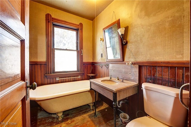 full bathroom with toilet, a wainscoted wall, wood finished floors, and a soaking tub