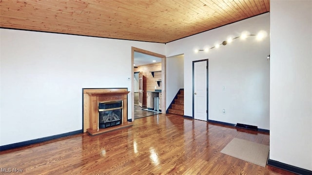 unfurnished living room featuring a glass covered fireplace, wood finished floors, wooden ceiling, baseboards, and stairs