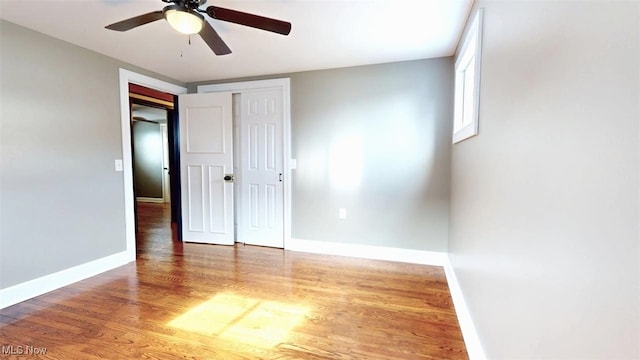 unfurnished bedroom with a closet, wood finished floors, a ceiling fan, and baseboards