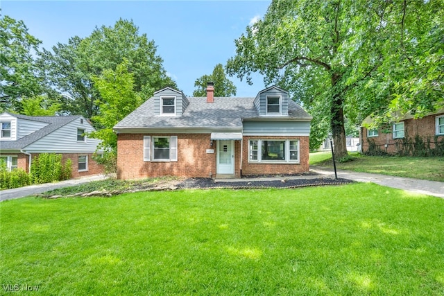 cape cod-style house with roof with shingles, brick siding, a chimney, and a front yard