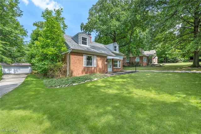 new england style home with an outbuilding, brick siding, a front yard, and a shingled roof