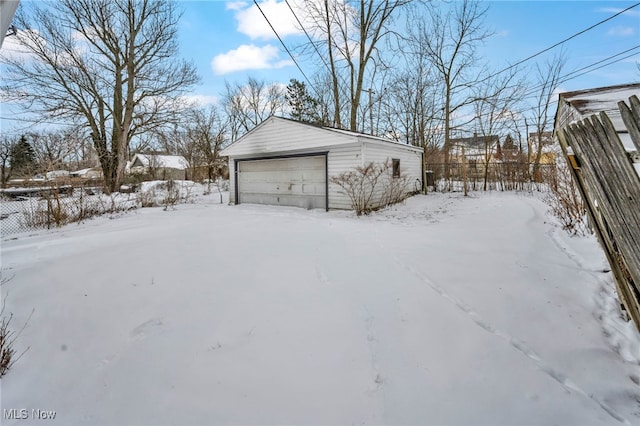 snow covered garage featuring a detached garage and fence