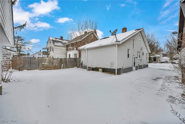 snow covered back of property featuring a chimney and fence