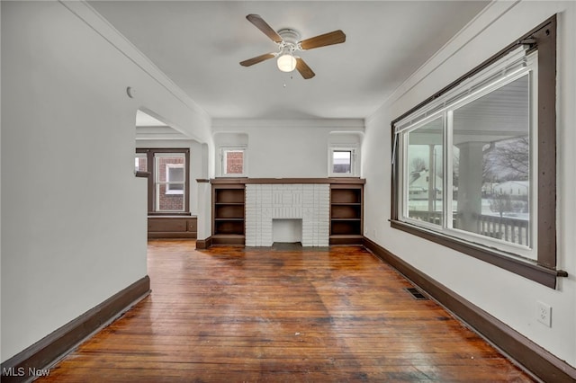 unfurnished living room featuring dark wood-style floors, a wealth of natural light, ornamental molding, and baseboards