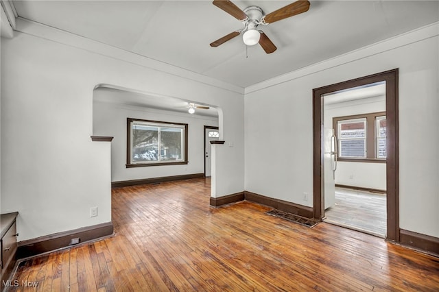 empty room featuring a ceiling fan, crown molding, baseboards, and wood finished floors