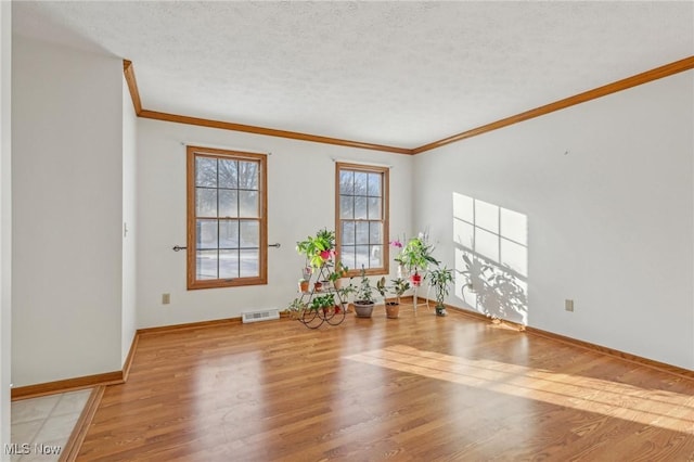 unfurnished room featuring crown molding, visible vents, a textured ceiling, light wood-type flooring, and baseboards