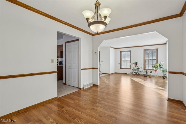 empty room with light wood-style floors, baseboards, crown molding, and an inviting chandelier