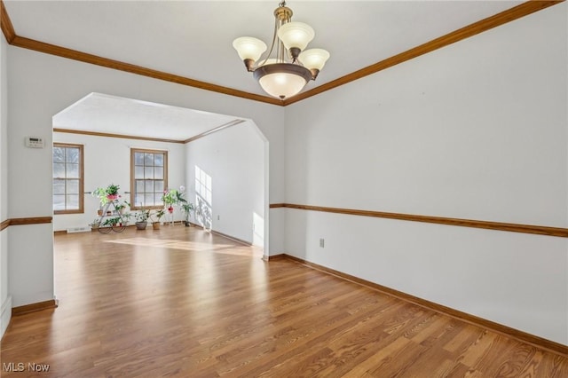 spare room with arched walkways, a notable chandelier, baseboards, light wood-style floors, and ornamental molding