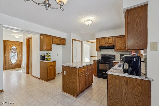 kitchen with under cabinet range hood, a kitchen island, backsplash, brown cabinets, and black electric range oven