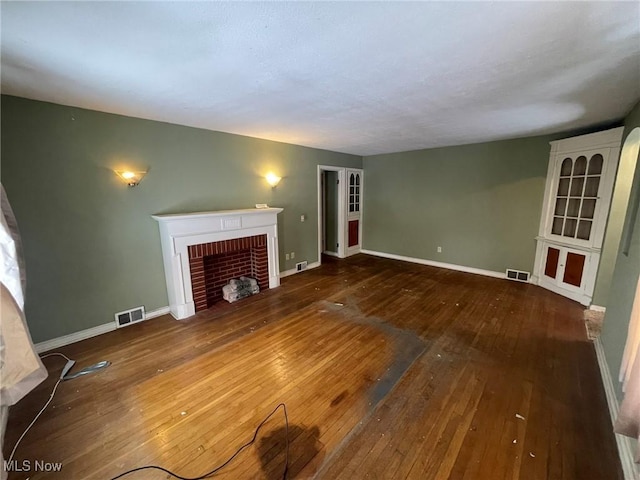 unfurnished living room with a fireplace, wood finished floors, visible vents, and baseboards