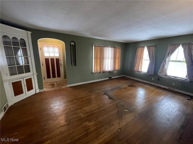 unfurnished living room with dark wood-style floors, baseboards, and visible vents